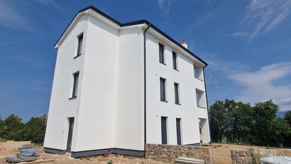 Bâtiment de trois étages enduit en blanc avec fenêtres sombres et mur en pierre