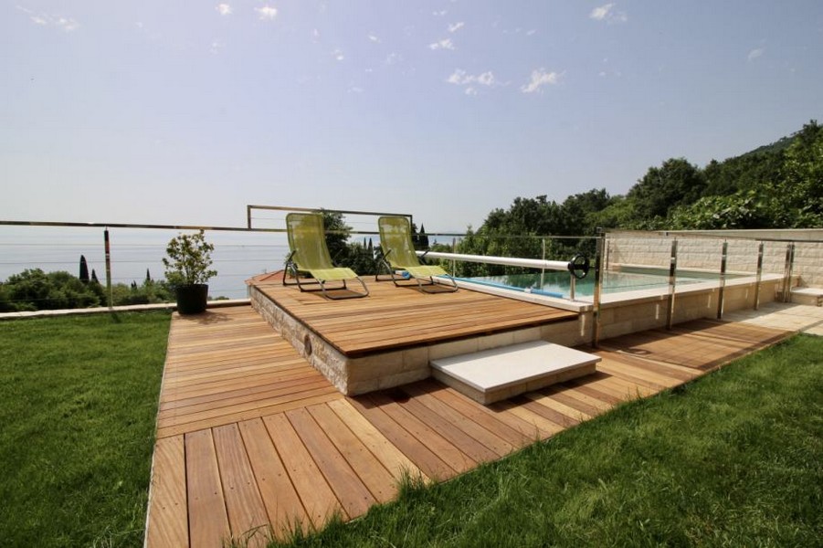 Terrasse en bois avec bains de soleil au bord de la piscine au-dessus de la mer