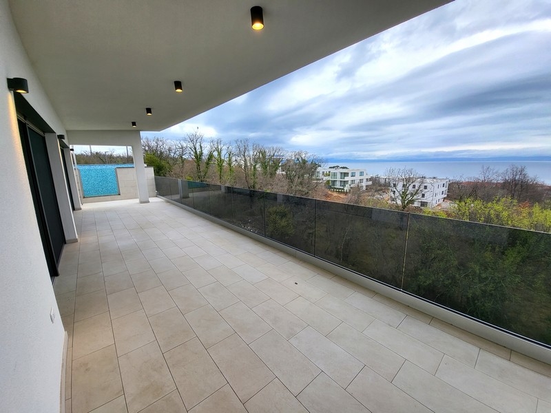 Large terrasse avec garde-corps en verre et vue sur la mer au-dessus des arbres
