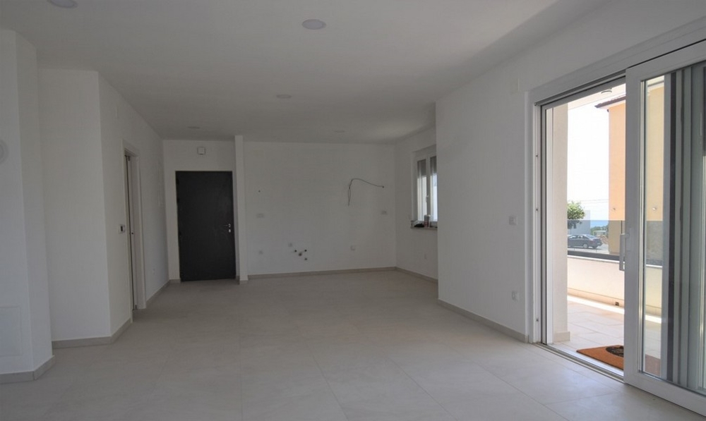 Séjour vide avec porte d'appartement et sortie sur la terrasse