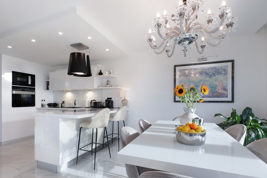 Cuisine blanche avec îlot de cuisson et lustre au-dessus de la table à manger