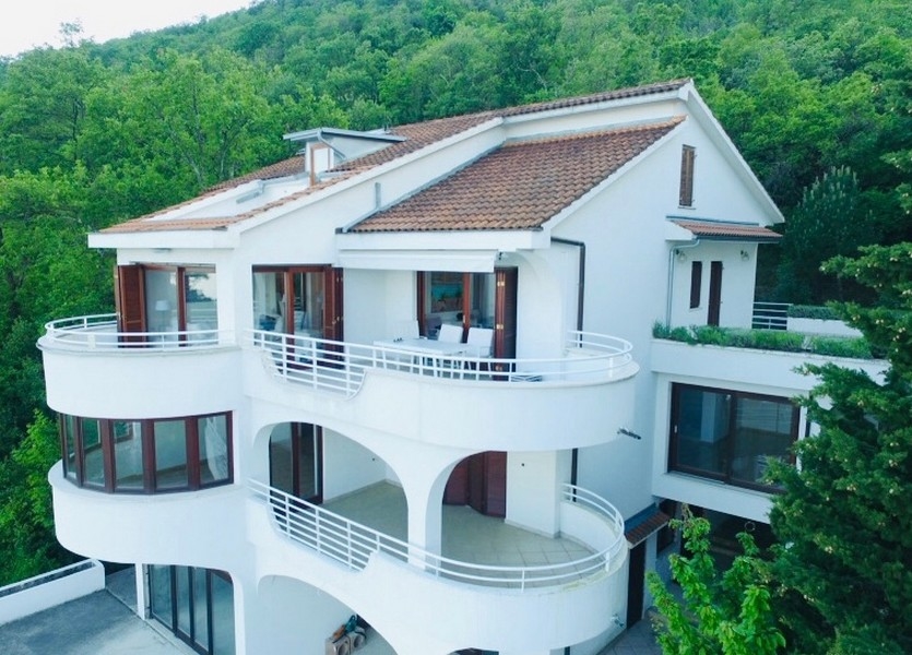 Maison blanche avec balcons ronds devant le versant boisé