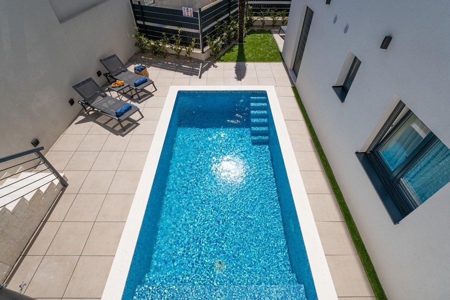 Piscine avec transats vue d'en haut entre le mur de la maison et la clôture