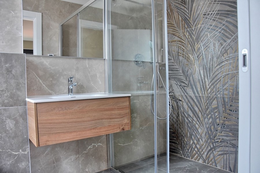 Salle de bains moderne dans un penthouse en Istrie avec une cabine de douche aux carreaux de verre décoratifs et un meuble-lavabo en bois.