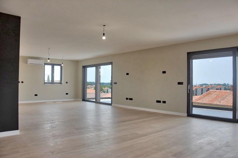 Penthouse moderne en Istrie avec séjour vide, plusieurs prises électriques et grandes fenêtres.
