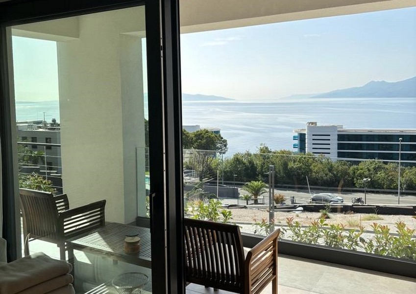 Balcon avec chaises en bois et vue mer par une porte vitrée ouverte, offre immobilière à Rijeka, Croatie.