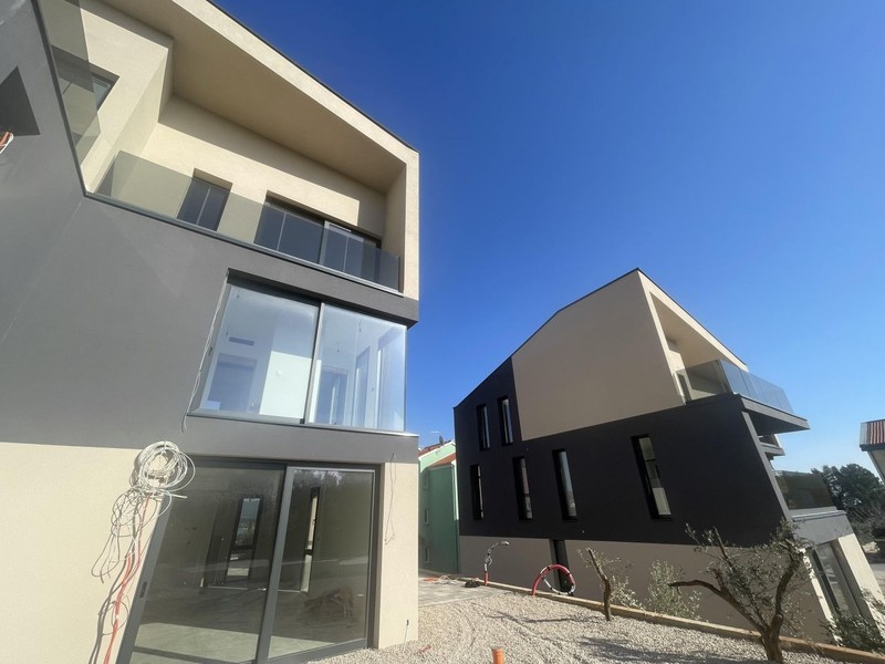 Deux immeubles neufs avec garde-corps en verre et oliviers dans un jardin de gravier