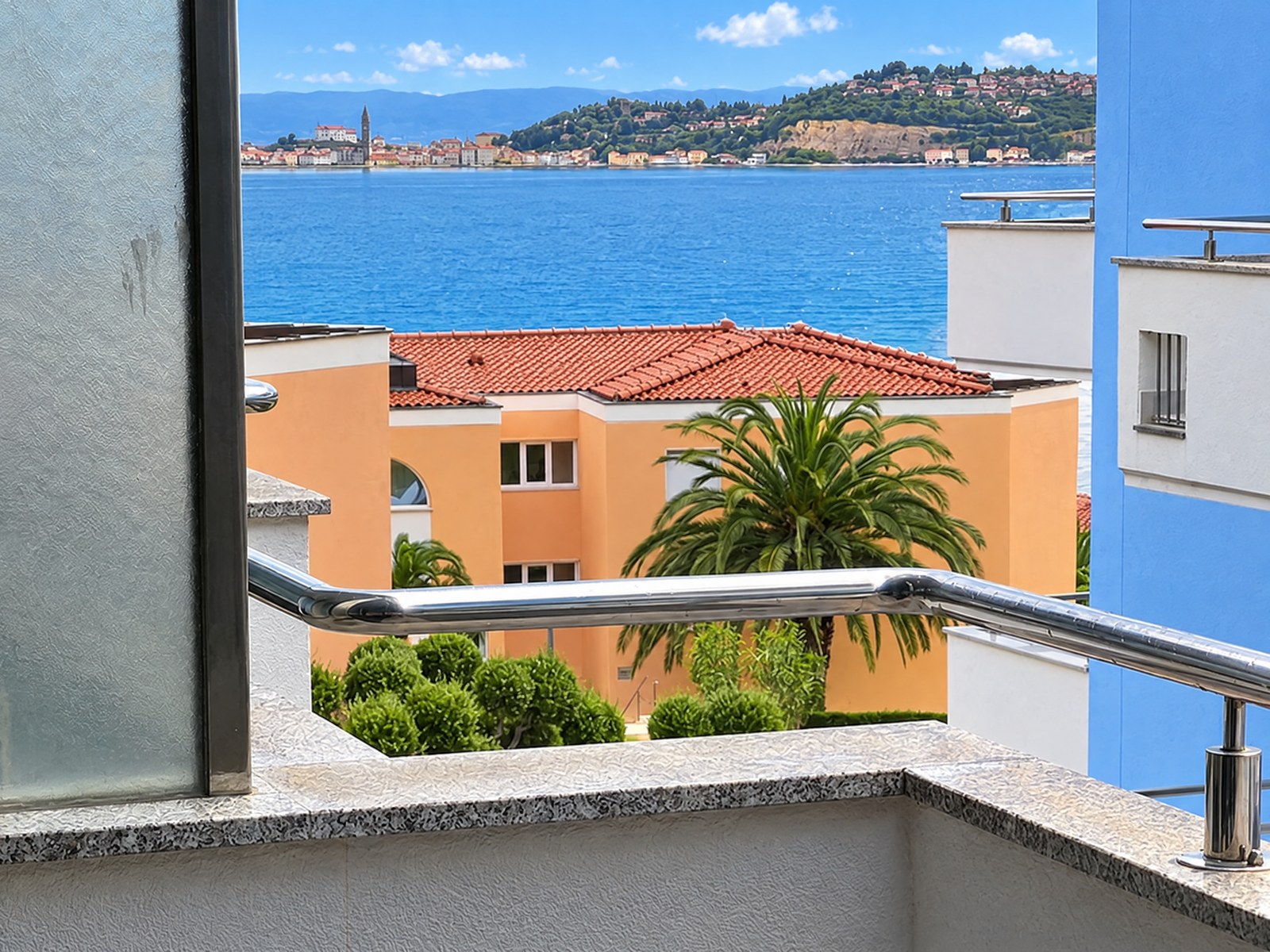 Vue depuis le balcon sur un palmier et les toits jusqu'à la mer