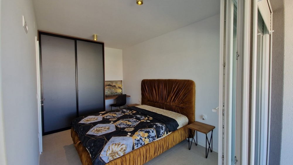 Chambre d'un appartement à Novalja, île de Pag, avec lit brun et accès à un balcon, biens immobiliers Croatie