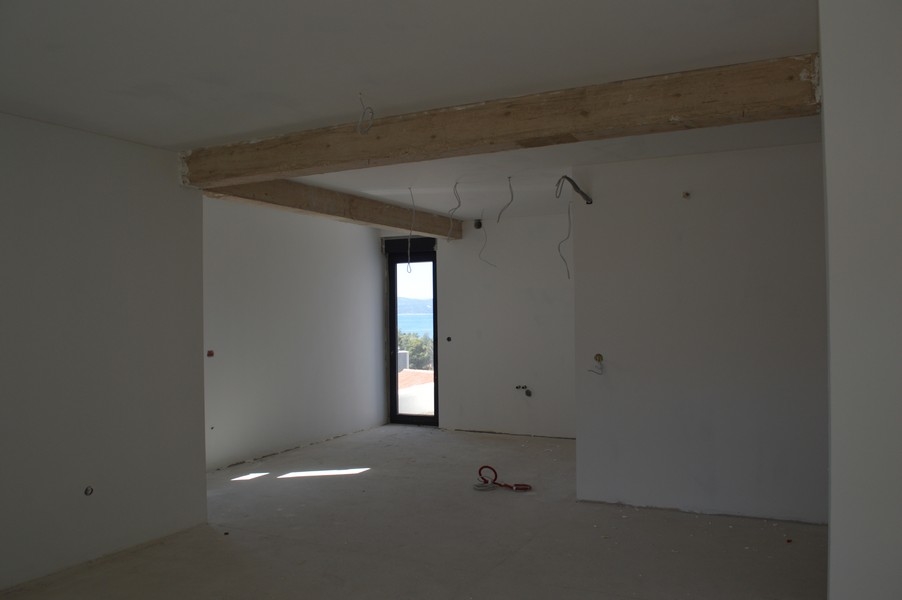 Spacieux salon dans un appartement inachevé avec poutres en bois apparentes et vue sur la mer.