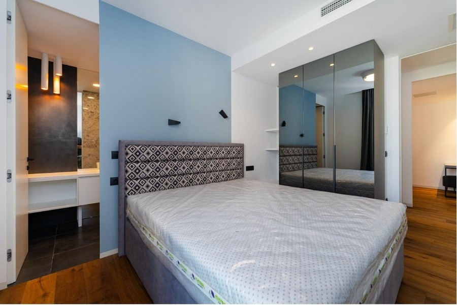 Chambre avec murs bleu et blanc, lit gris, armoire à miroir