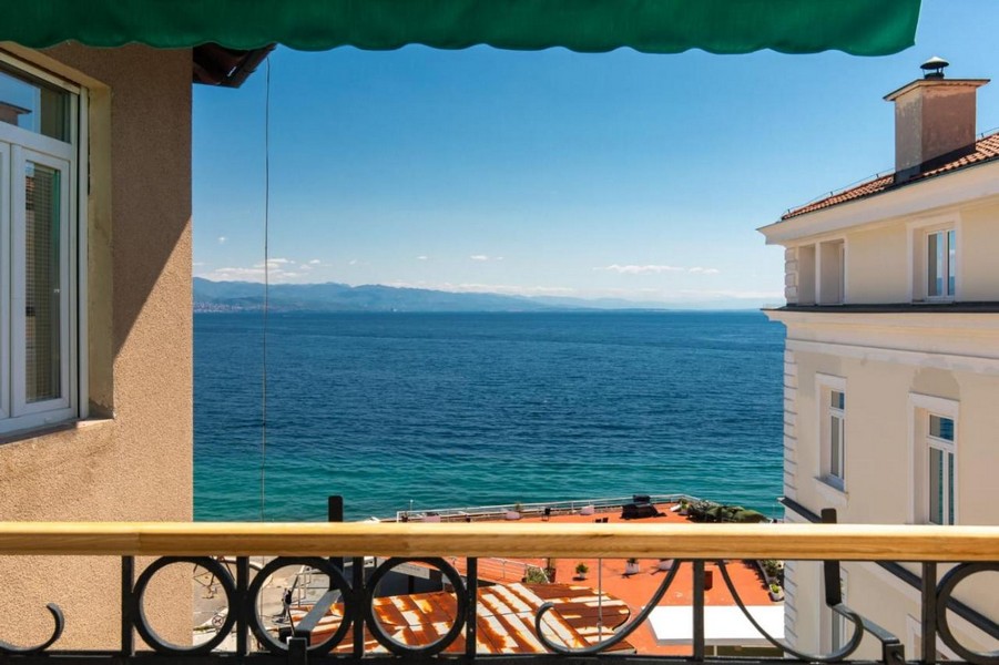 Balcon sous un store vert avec vue sur l'eau turquoise