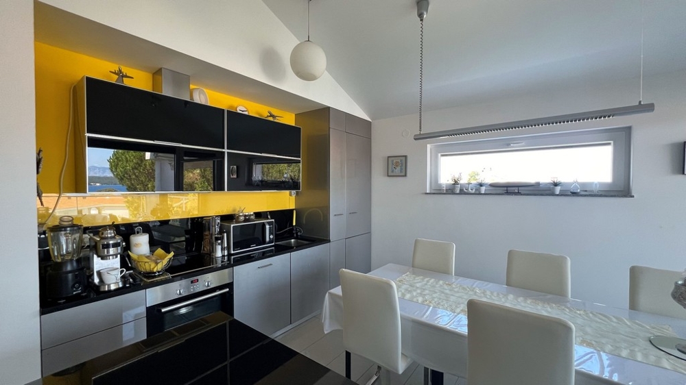 Cuisine moderne avec plan de travail noir et crédence jaune, coin repas attenant.