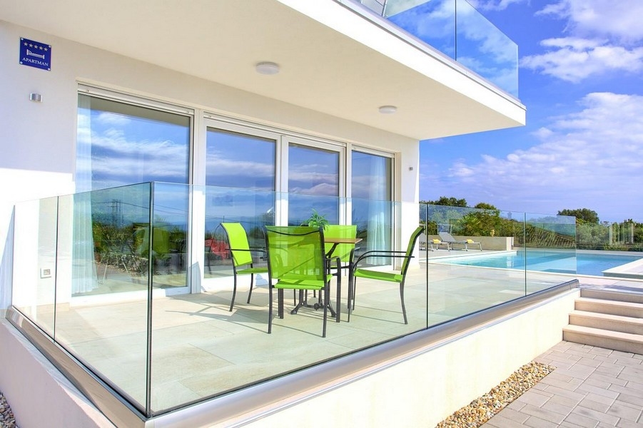 Terrasse avec chaises vertes et garde-corps en verre à côté de la piscine