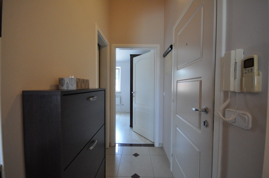 Couloir avec porte blanche, armoire sombre et interphone au mur, accès à différentes pièces