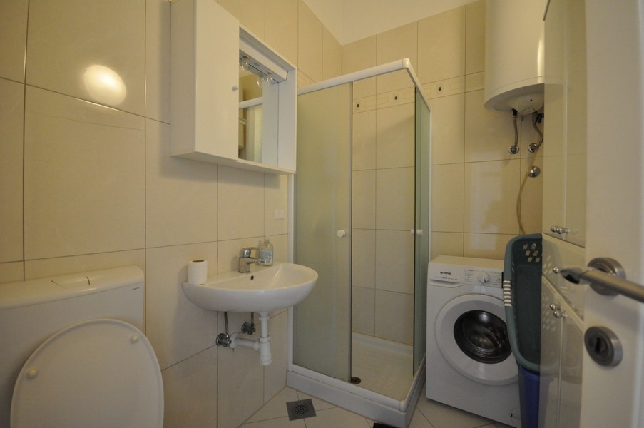 Salle de bains avec douche, lavabo, WC et lave-linge, murs et sol carrelés en tons clairs
