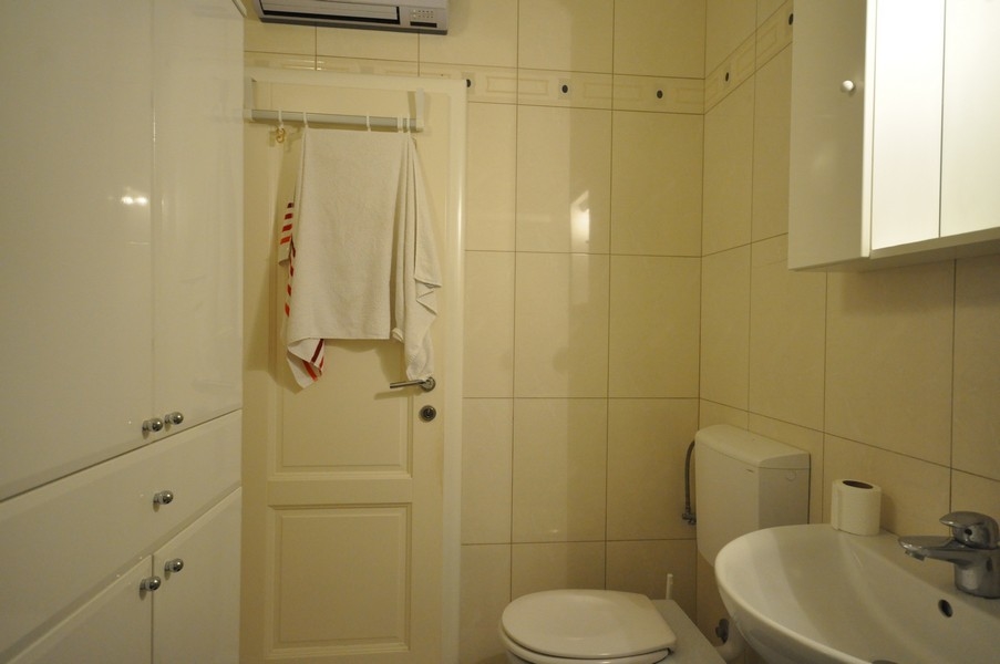 Salle de bains avec WC, lavabo, porte-serviettes sur la porte, carrelage clair, équipement moderne