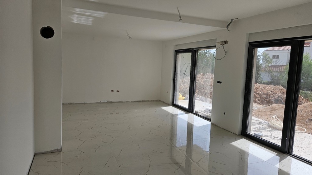 Intérieur avec grande baie vitrée, murs blancs et carrelage au sol, encore en construction.