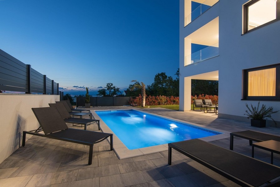 Vue de nuit de la piscine éclairée avec chaises longues