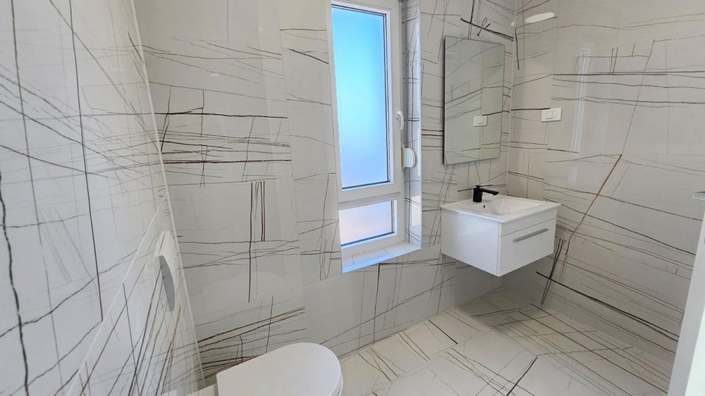 Salle de bains au carrelage moderne avec fenêtre, lavabo et WC