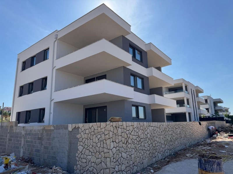 Immeuble neuf avec bandeaux de balcons blancs derrière le mur en pierre naturelle