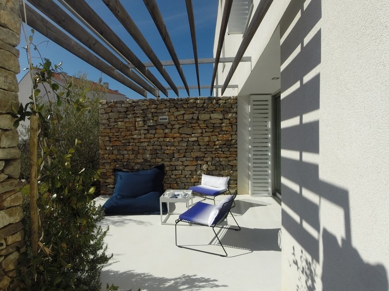 Terrasse sous la pergola avec pouf devant le mur en pierres sèches
