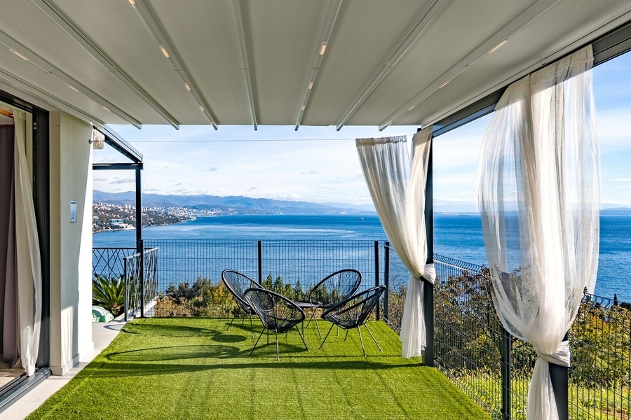 Loggia avec gazon synthétique, rideaux et fauteuils en fil métallique au bord de la mer