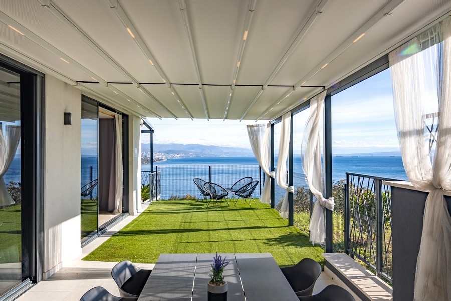 Terrasse couverte avec jardin et vue mer panoramique.