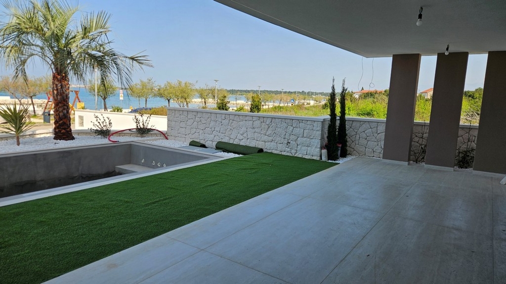Terrasse avec gazon synthétique et palmier devant le mur en pierre naturelle