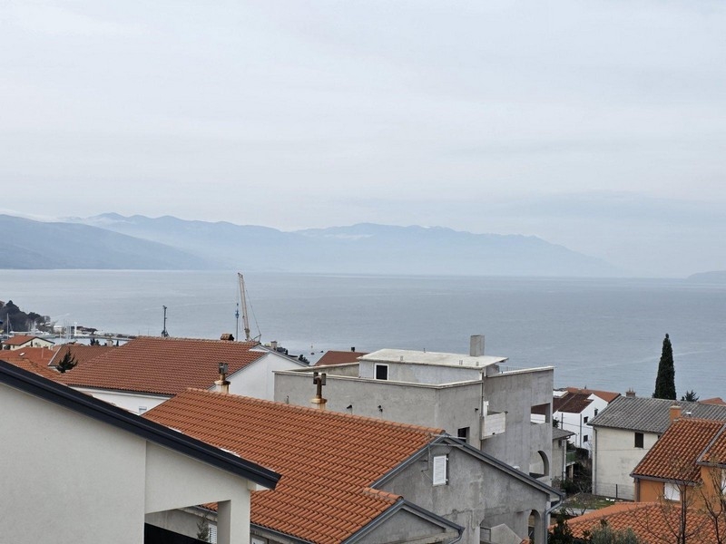 Toits de tuiles devant la baie embrumée avec une grue sur le rivage