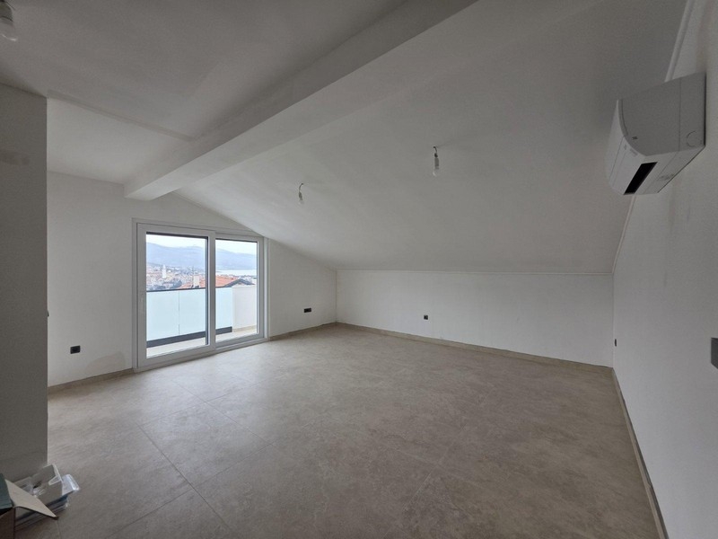 Pièce vide sous les combles avec porte du balcon et vue sur la baie