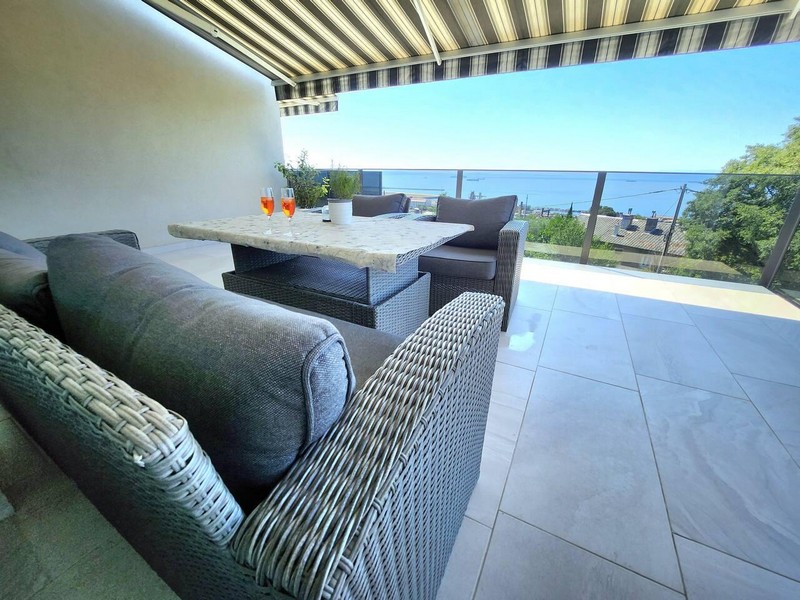 Terrasse couverte avec canapé en rotin, table à manger et vue mer