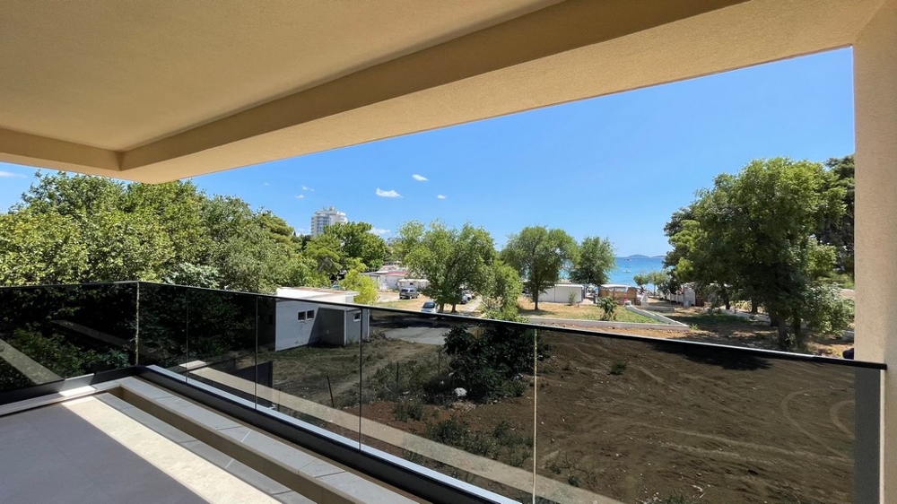 Balcon avec garde-corps en verre et vue à travers les arbres vers la plage