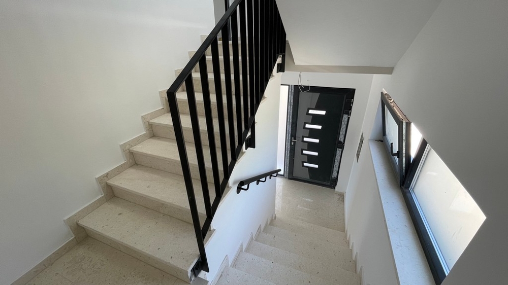 Cage d'escalier avec sol en pierre claire et rampe noire