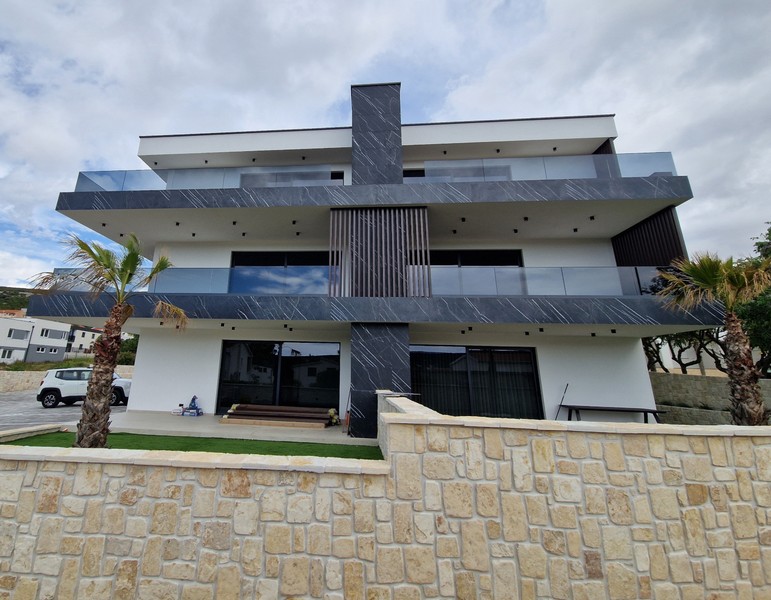 Immeuble neuf moderne avec garde-corps en verre et mur en pierre naturelle à Stara Novalja, île de Pag