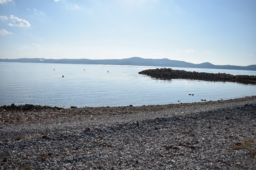 Plage de galets avec môle en pierre et collines à l'horizon