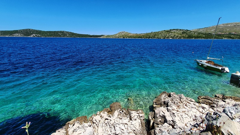 Eau turquoise avec voilier devant le rivage rocheux