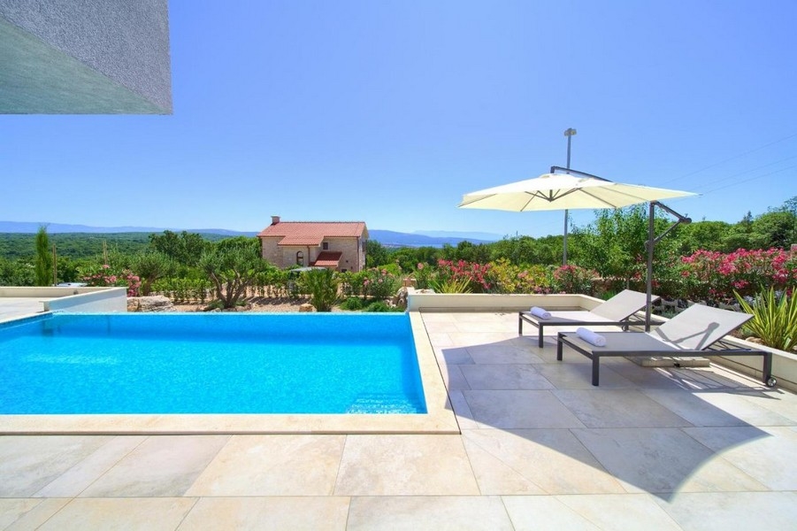 Piscine avec bains de soleil et parasol devant un jardin fleuri sur Krk
