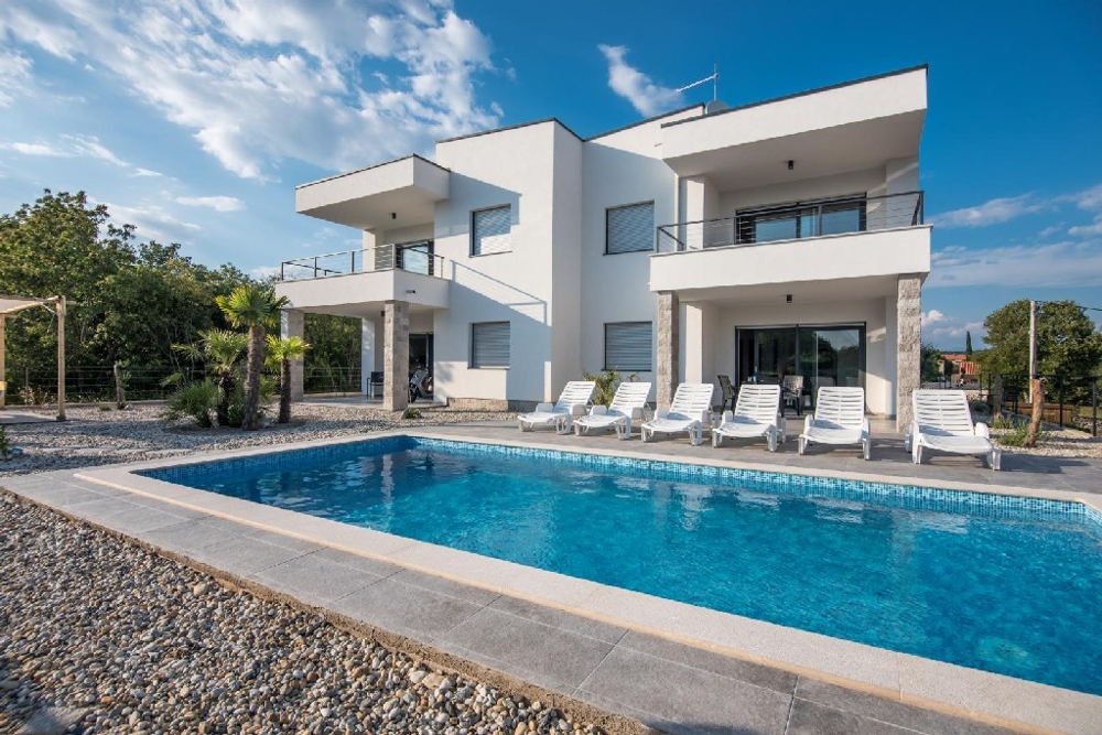 Villa blanche avec piscine et rangée de bains de soleil dans le jardin de gravier