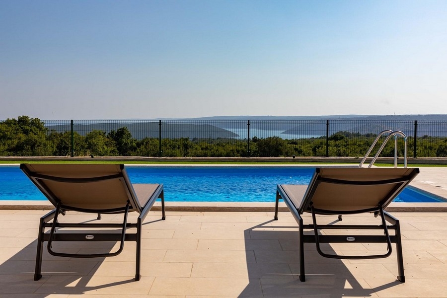 Deux bains de soleil au bord de la piscine avec vue sur le maquis jusqu'à la baie
