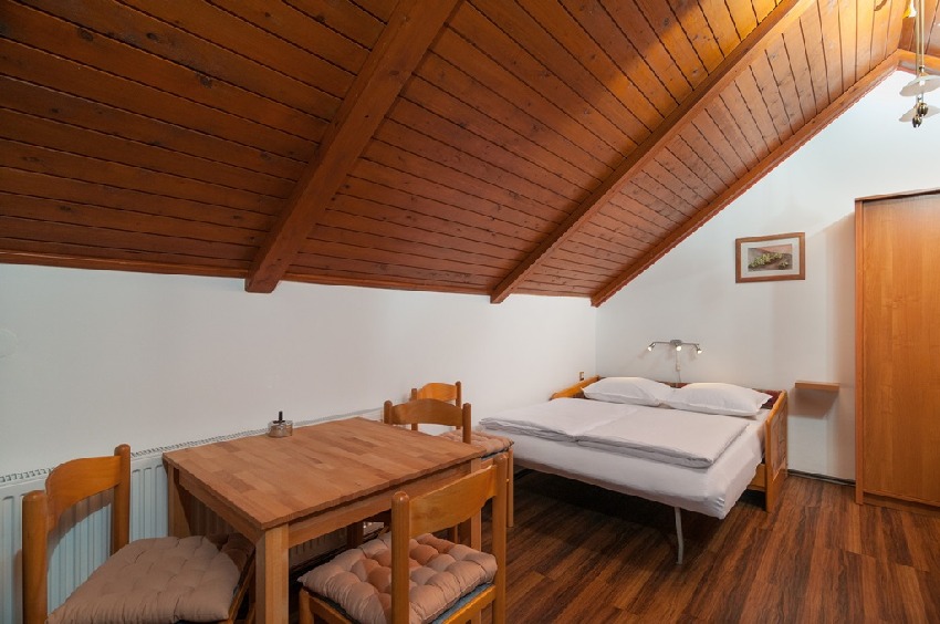 Chambre sous les combles avec plafond en bois, lit double et table à manger