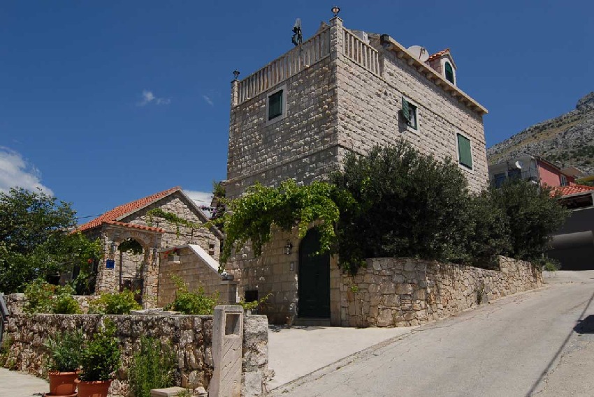 Maison en pierre avec volets verts et feuillage de vigne au bord de la route