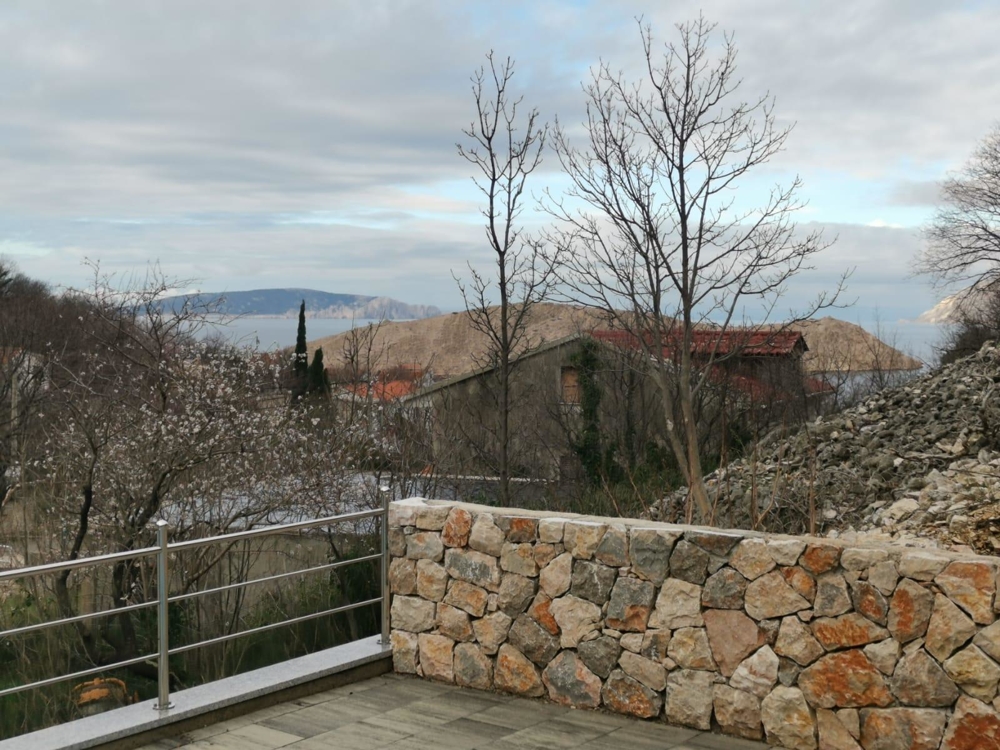 Terrasse avec mur en pierre naturelle et arbres dénudés devant la baie