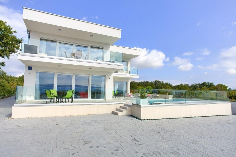 Villa blanche avec garde-corps en verre et piscine derrière une paroi en verre