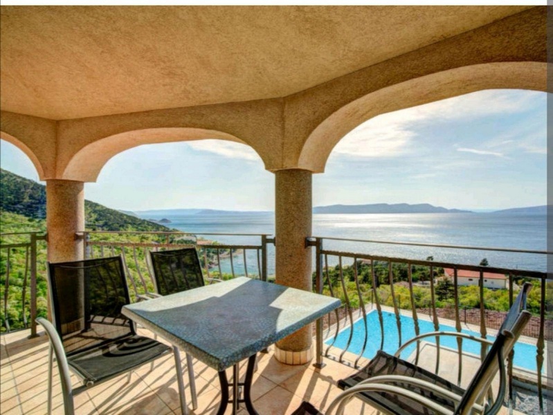 Loggia avec arcs et table en pierre au-dessus de la piscine et de la baie