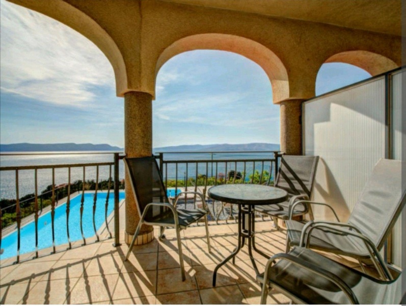 Vue sur la piscine et la mer depuis la terrasse couverte à l'étage.