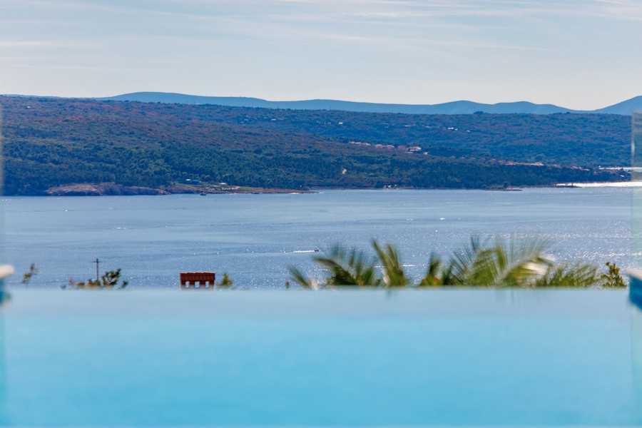 Espace repas couvert avec grill barbecue et vue sur la piscine et la mer.