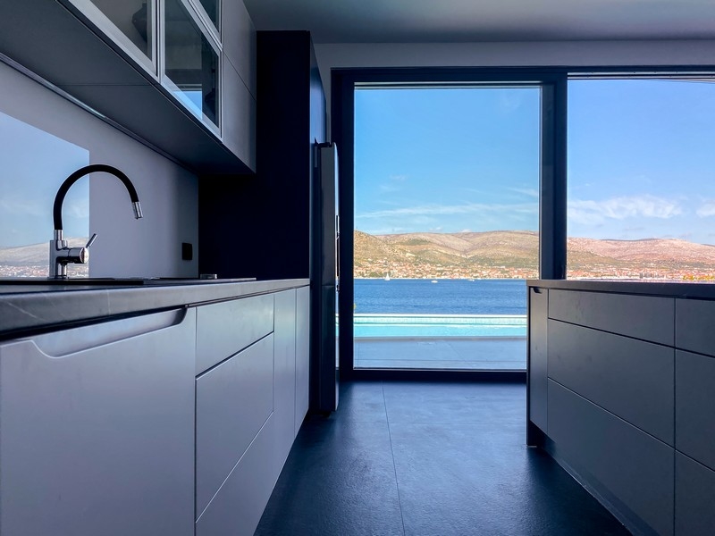 Cuisine équipée blanche avec porte ouverte sur la terrasse de la piscine