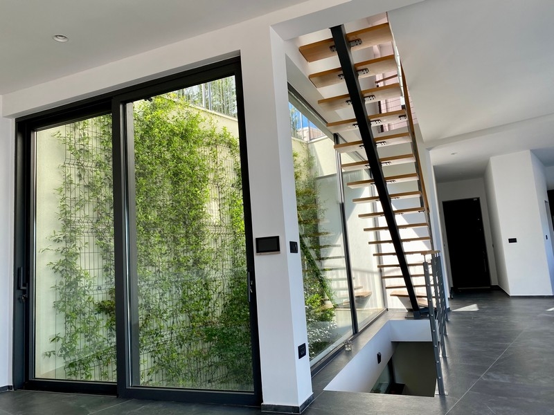 Entrée avec escalier ouvert en bois et puits de lumière végétalisé