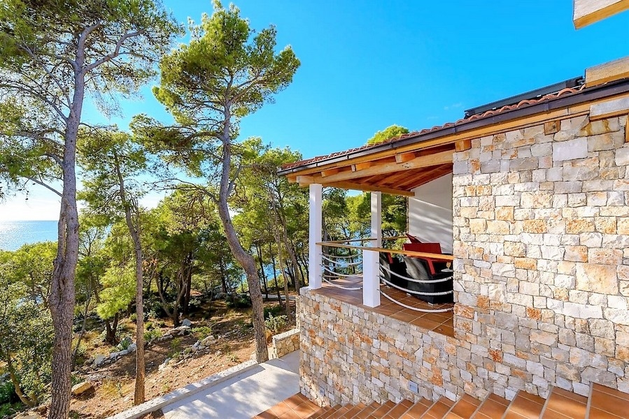 Maison en pierre avec terrasse couverte entre des pins au bord de la mer